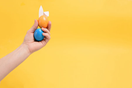 painted colorful eggs in hand with rabbit ears for easter holiday yellow background. background for...