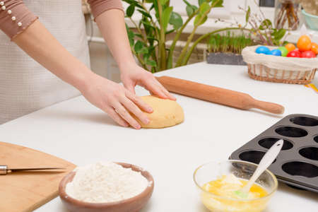 the process of rolling out the dough at home on the table is the hands of a woman for making cruffins festive pastries for Easter. side view of a bright kitchen, with painted eggs.の写真素材