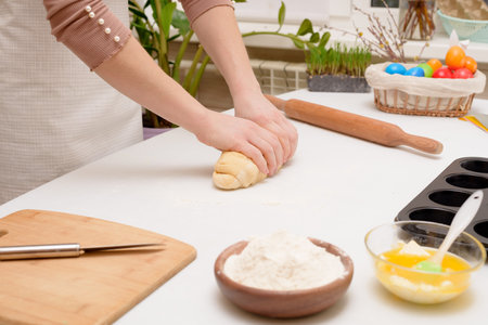 the process of rolling out the dough at home on the table is the hands of a woman for making cruffins festive pastries for Easter. side view of a bright kitchen, with painted eggs.の写真素材