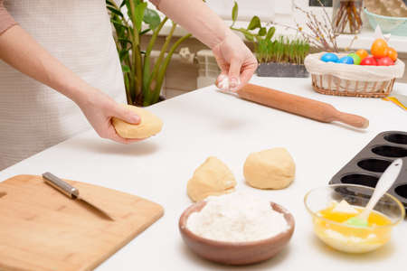 the process of rolling out the dough at home on the table is the hands of a woman for making cruffins festive pastries for Easter. side view of a bright kitchen, with painted eggs.の写真素材