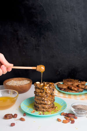 homemade oatmeal banana pancakes with chia seeds, almonds, prunes and dates, drizzled with honey and crushed nuts on a dark background. diet breakfast is healthy for the figure. levitation honey.の写真素材