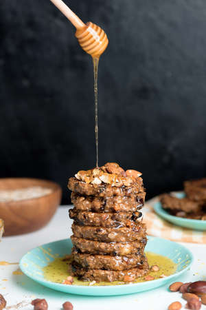 homemade oatmeal banana pancakes with chia seeds, almonds, prunes and dates, drizzled with honey and crushed nuts on a dark background. diet breakfast is healthy for the figure. levitation honey.の写真素材