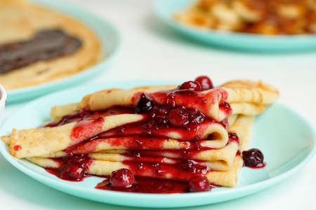 blini pancakes with red berry jam close-up on a blue plate on a light background. traditional Russian holiday is a symbol of spring and sweet dessert.の写真素材