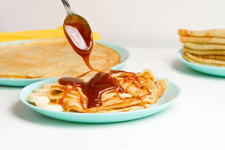 blini pancakes with caramel, dripping on a spoon levitation close-up on a blue plate on a light background. traditional Russian holiday is a symbol of spring and sweet dessert.の写真素材