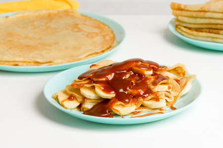 blini pancakes with caramel, dripping on a spoon levitation close-up on a blue plate on a light background. traditional Russian holiday is a symbol of spring and sweet dessert.の写真素材