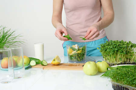 step-by-step recipe for making smoothies from micro-green apples cucumber and spinach. woman hands cut vegetables and put them in blender for whipping eco organic fresh food detox on light backgroundの写真素材
