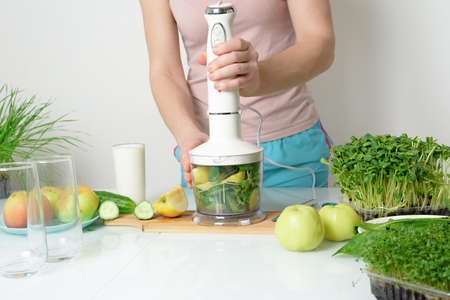 step-by-step recipe for making smoothies from micro-green apples cucumber and spinach. woman hands cut vegetables and put them in blender for whipping eco organic fresh food detox on light backgroundの写真素材