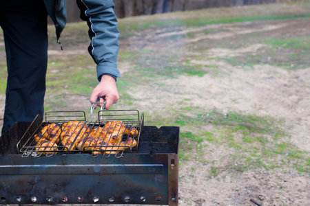 barbecue in nature in the spring. a mans hand holds a grate of meat over the coalsの写真素材
