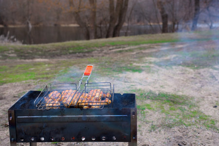 barbecue in nature in the spring. a mans hand holds a grate of meat over the coalsの写真素材