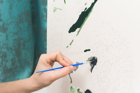 hobbies at home self-isolation, painting by numbers to draw from the top view of a woman holding a brush with paints, painting. the home interior is light.のeditorial素材