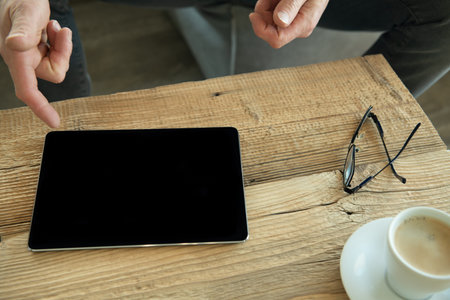 Table with tablet, coffee and glasses. Man points finger at tablet.