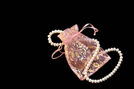 White pearls in lacy handbag on the black silk background の写真素材