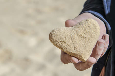 Man hand hold a heart shaped sea sand in a beachの写真素材