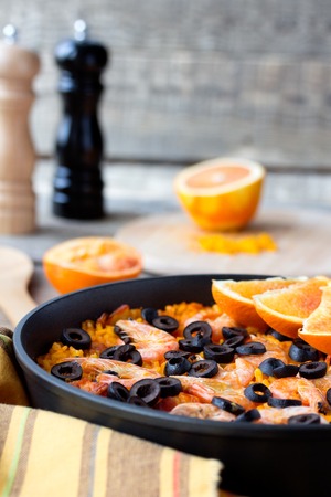 Tradition Spanish dish - valencian seafood Paella in authentic pan paellera with black pepper mill and red orange fruit.の写真素材
