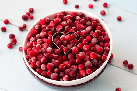 Frozen Cranberries in Bowl within heart shaped cookie cutter on painted wooden tableの写真素材