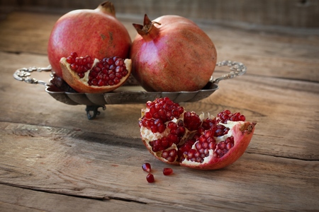 Three red juicy pomegranate on plate lying on wooden table from old boardsの写真素材