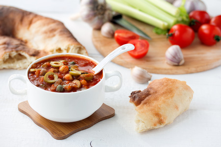 thick vegetable soup in a white bowl on wooden table surrounded by bread, greens and vegetablesの写真素材