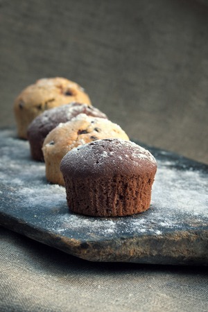 four chocolate and vanilla muffin on rustic bakery peel with sugar powderの写真素材