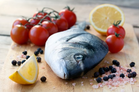 fresh gilt-head bream fish on cutting board with lemon and tomatoの写真素材