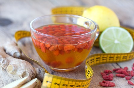 Cup of delicious dietary Goji berry tea on wooden desk with lime, lemon, ginger and yellow sartorial meterの写真素材