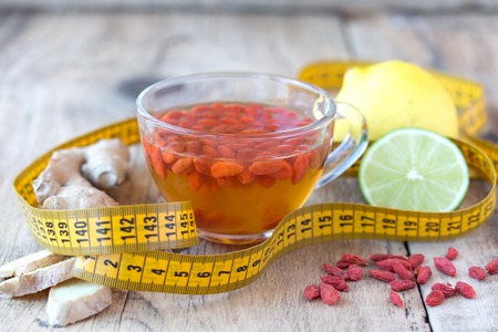 Cup of delicious dietary Goji berry tea on wooden desk with lime, lemon, ginger and yellow sartorial meterの写真素材