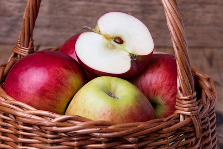 Fresh red apples in wicker basket over wooden backgroundの写真素材