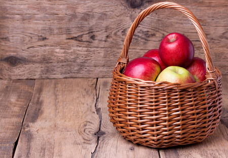 Fresh red apples in wicker basket over wooden background. Copyspace.の写真素材