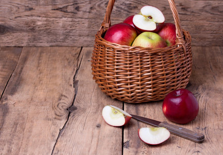 Fresh red apples in wicker basket with fruit knife over wooden background. Copyspace.の写真素材