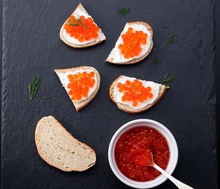 Bread with fresh cream cheese and red caviar on black slate plateの写真素材