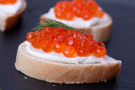 Bread with fresh cream cheese and red caviar on black slate plateの写真素材
