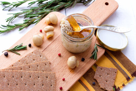 Chicken pate in jar and crispbread with champignon and rosemary on wood cutting boardの写真素材