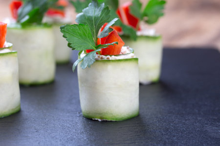 Cucumber spring rolls with soft cheese, parsley and red bell pepper on black slate plate