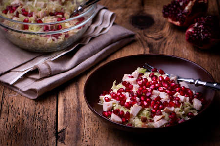 Healthy salad with pomegranate seeds, chicken and cabbage. Old wooden table. Low key.の写真素材