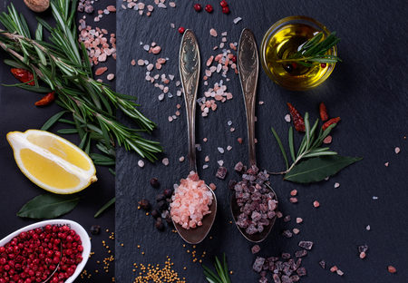Black salt and Pink Himalayan salt in spoons. Various spices on black slate desk.の写真素材