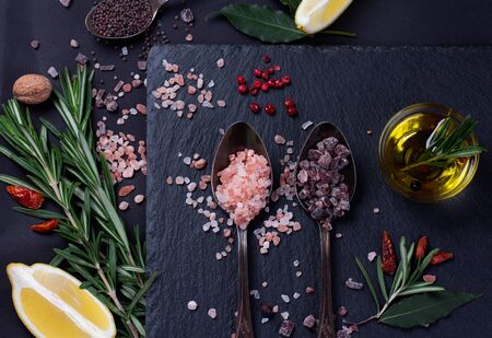 Black salt and Pink Himalayan salt in spoons. Various spices on black slate desk.の写真素材