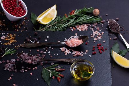 Black salt and Pink Himalayan salt in spoons. Various spices on black slate desk.の写真素材
