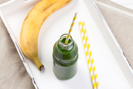Healthy green smoothie made from spinach, kiwi, bananas and mint in a jar with yellow straws on a wooden table.の写真素材