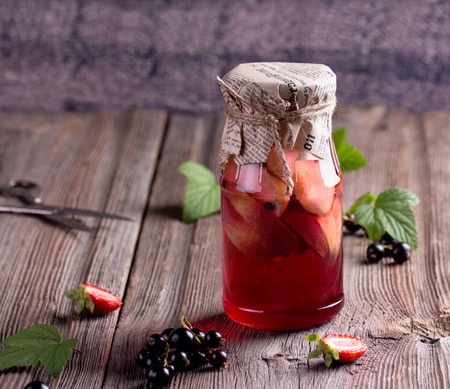 Canned homemade apple and berry compotes in glass jars. Old wooden desk. Rustic. Vintage.の写真素材