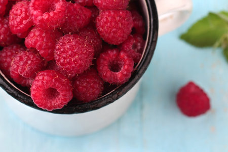 Raspberries in a enamel mug on blue wooden background. Top view.