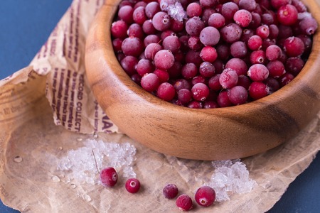 Close up of frozen cranberries. Healthy frozen berries in wooden bowl on old newspaper.の写真素材