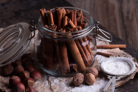 Cinnamon sticks in transparent glass jar. Nuts and sugar on rustic wooden background.の写真素材