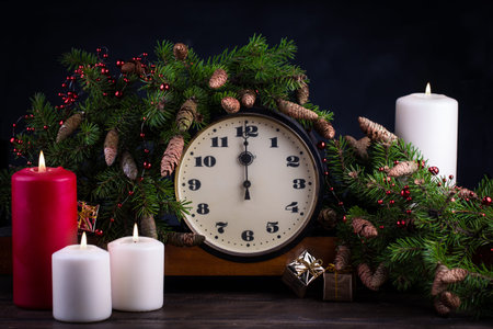 Happy New Year decoration. Vintage clock showing twelve. Candle and fir branch on woodtn background.の写真素材