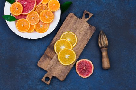 Fresh oranges, grapefruits and madarine slices on dark blue stone background. Rustic kitchen utensils: wooden cutting desk and squeezer. Top view with copy spaceの写真素材