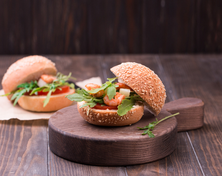 Asian burger with shrimps, arugula, tomato and onion with white sauce. Old wooden table.の写真素材