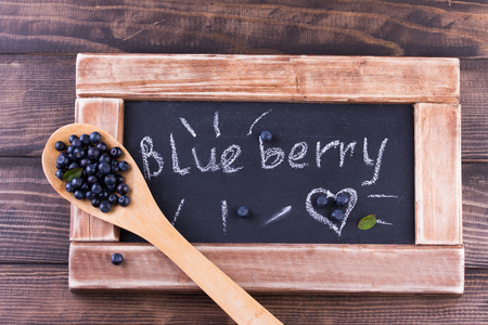 Blueberries in a wooden spoon on a vintage wooden table with black chalkboard. Healthy food concept.の写真素材