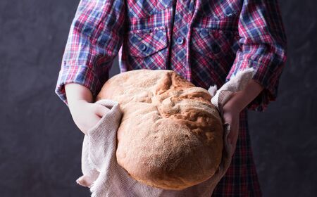 Little girl in plaid shirt holding freshly baked crusty homemade ciabatta bread. Dark backgroundの写真素材