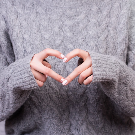 Closeup of young female in knitted sweater making heart shape with hands