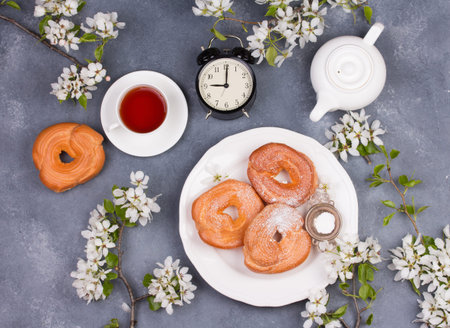 Powdered choux pastry with tea. Table decorated with apple blossom. Alarm clock as Time for...