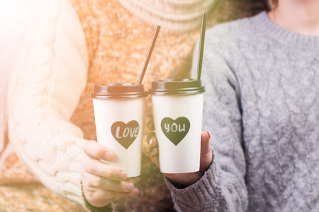 Young couple in warm sweaters and blue jeans with paper takeaway cups of coffee.の写真素材
