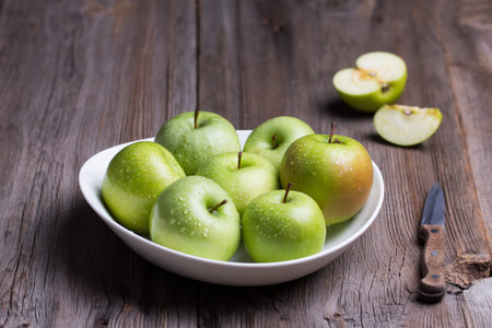 Green organic healthy apples in bowl on wooden board. Healthy food